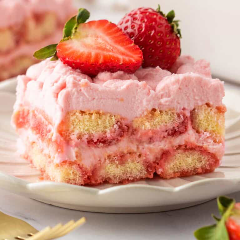 A slice of Strawberry Tiramisu (topped with fresh sliced strawberries) on a white plate.