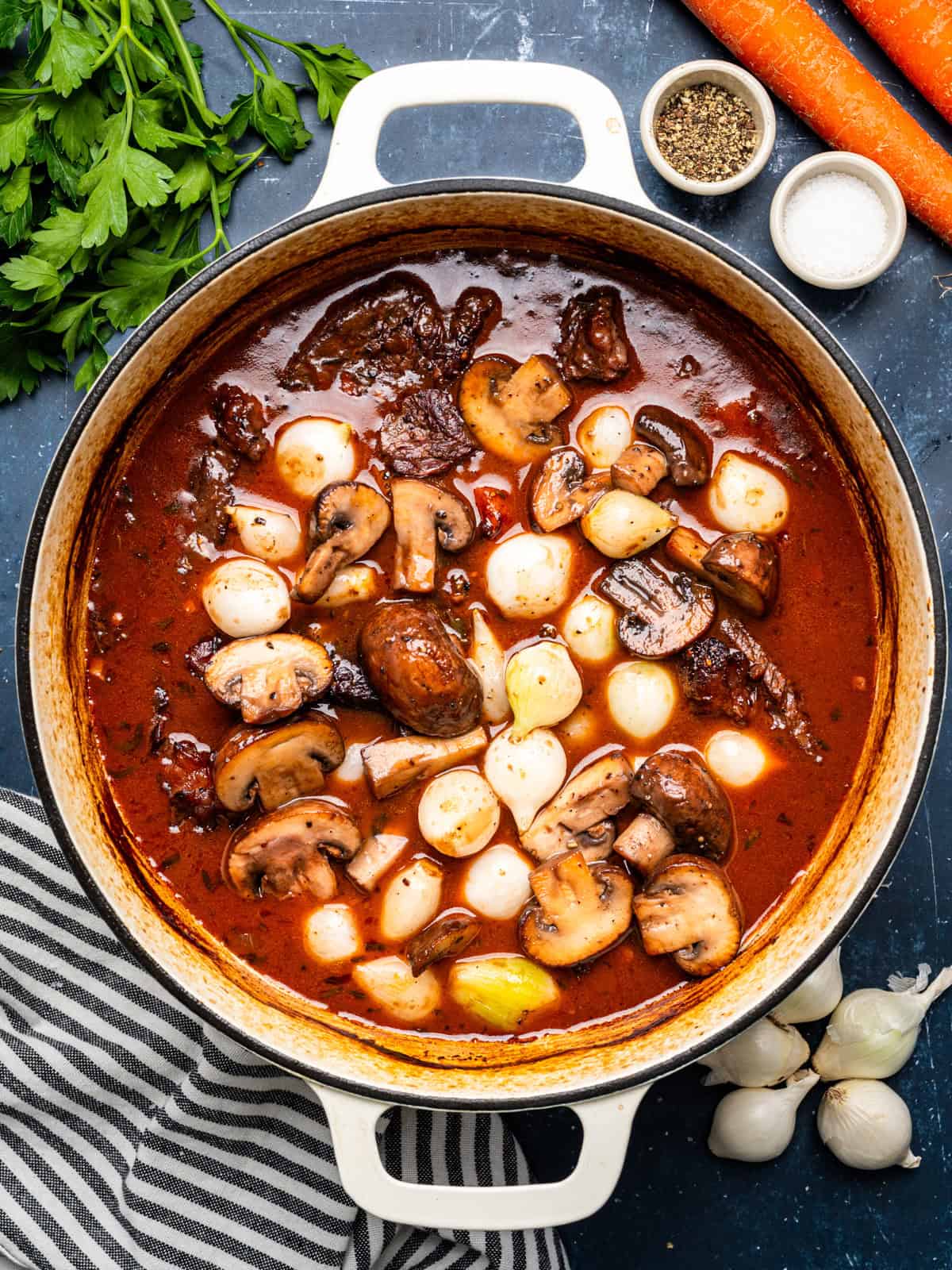 Beef Bourguignon with pearl onions and mushrooms in a large white Dutch oven.