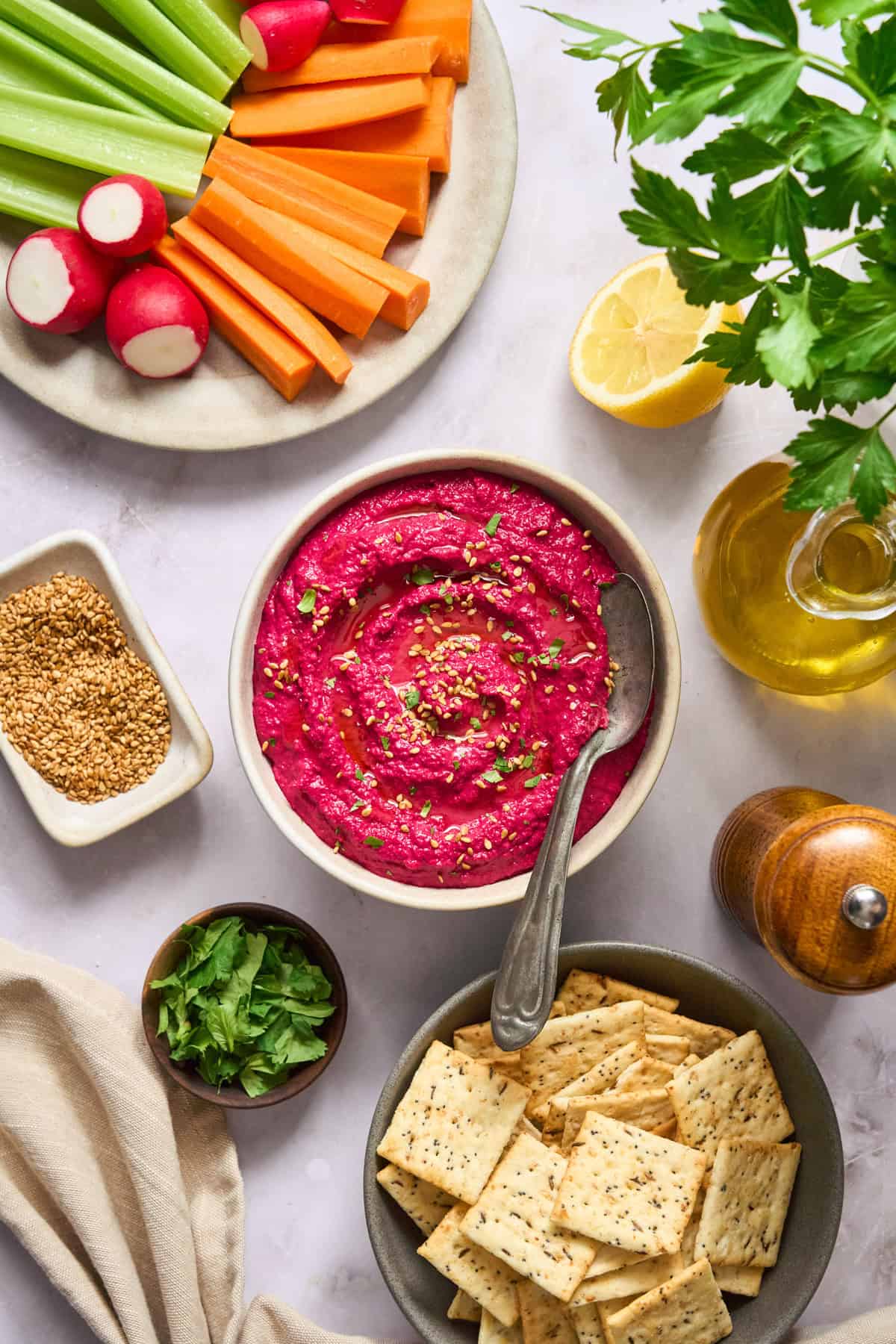 The overhead view of the beet hummus in a bowl together with a veggie bowl and a cracker bowl - on a white background.