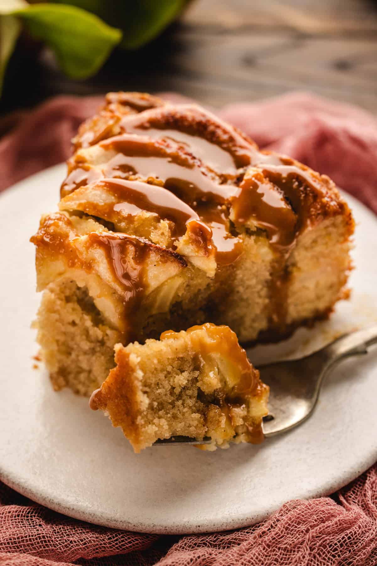 A slice of German Apple Cake drizzled with caramel sauce on a white plate, with a bite on a fork.