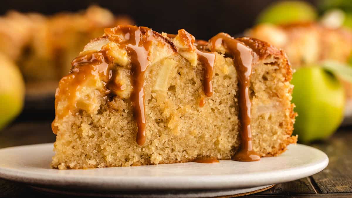 A slice of German Apple Cake drizzled with caramel sauce on a white plate.