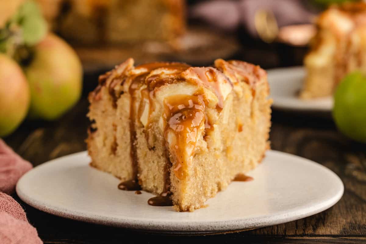 A slice of German Apple Cake drizzled with caramel sauce on a white plate.