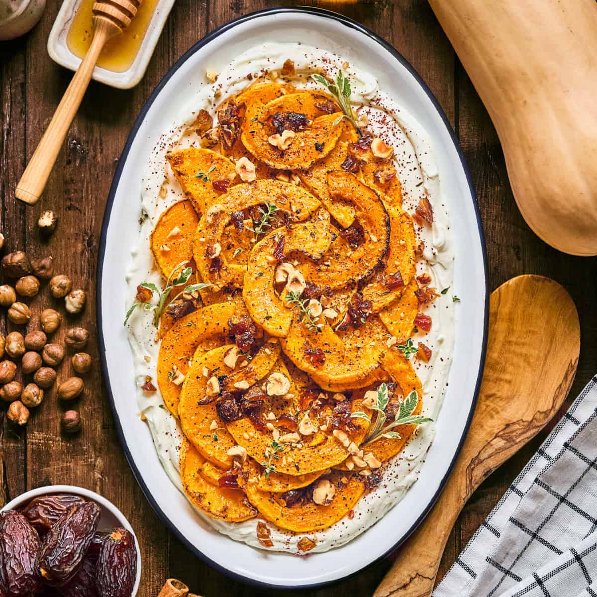 Roasted Butternut Squash with Honey Labneh, Dates, and Hazelnuts on a white platter.