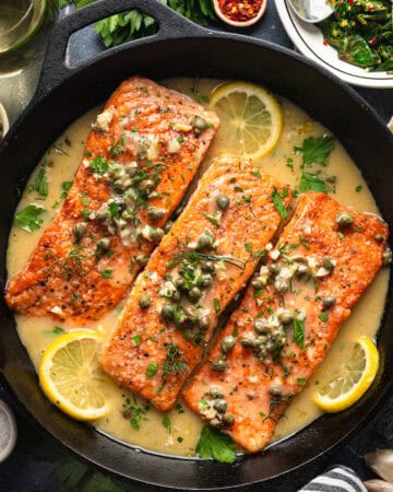 Salmon Piccata (3 salmon fillets topped with capers and surrounded by lemon slices) in a cast iron skillet.