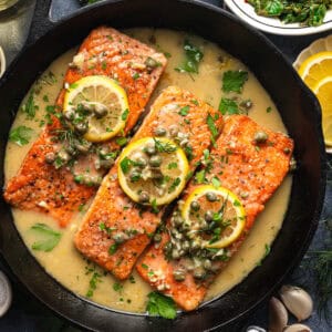 Salmon Piccata (3 salmon fillets topped with capers and lemon slices) in a cast iron skillet.