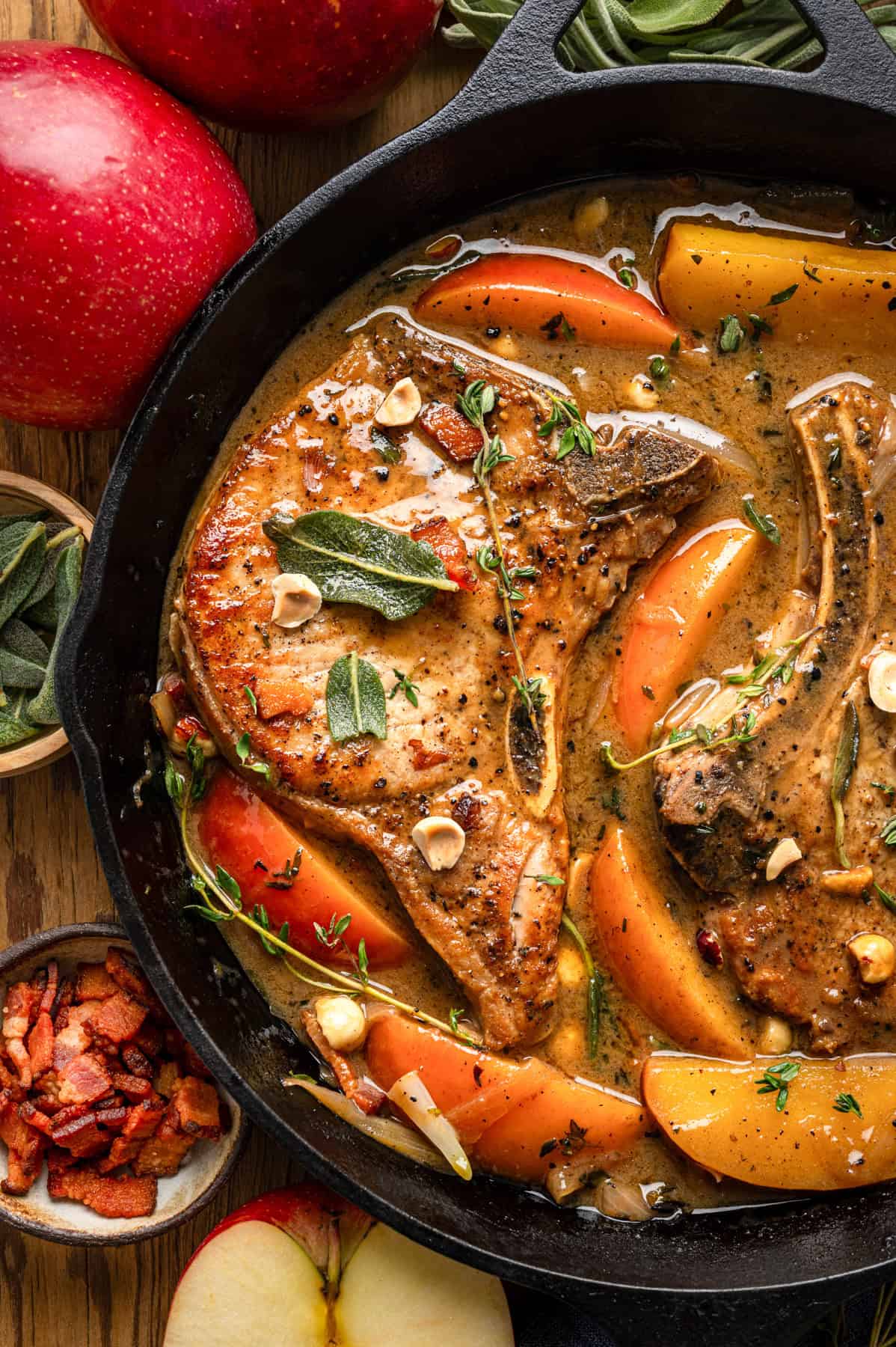 Apple Cider Pork Chops with Apples and Bacon Pork Chops with Apples, Bacon, and Hazelnuts in a black cast iron pan.