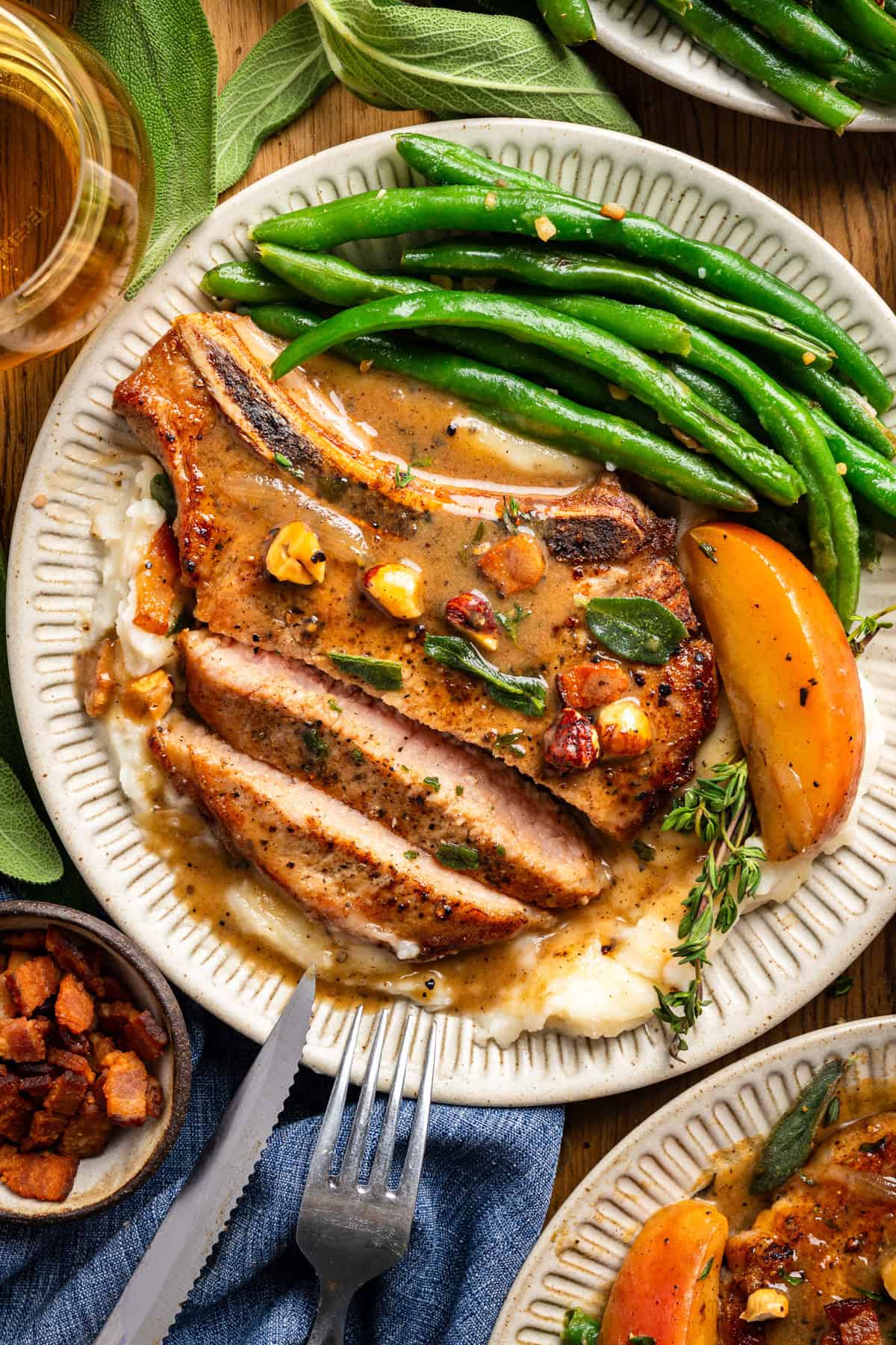 Apple Cider Pork Chops with Apples and Bacon Pork Chops with Apples, Bacon, Hazelnuts, green beans, and mashed potatoes - on a white plate.