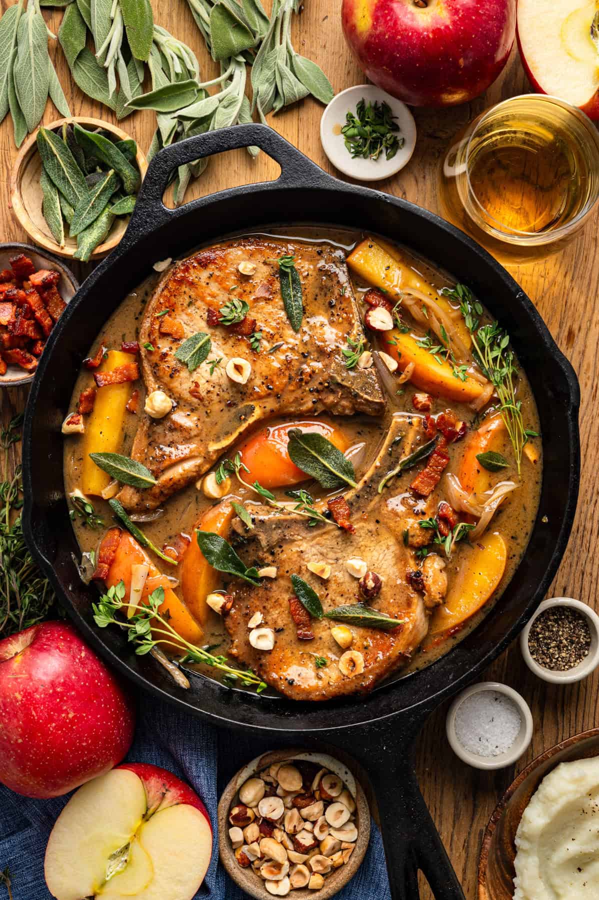 Apple Cider Pork Chops with Apples and Bacon Pork Chops with Apples, Bacon, and Hazelnuts in a black cast iron pan.