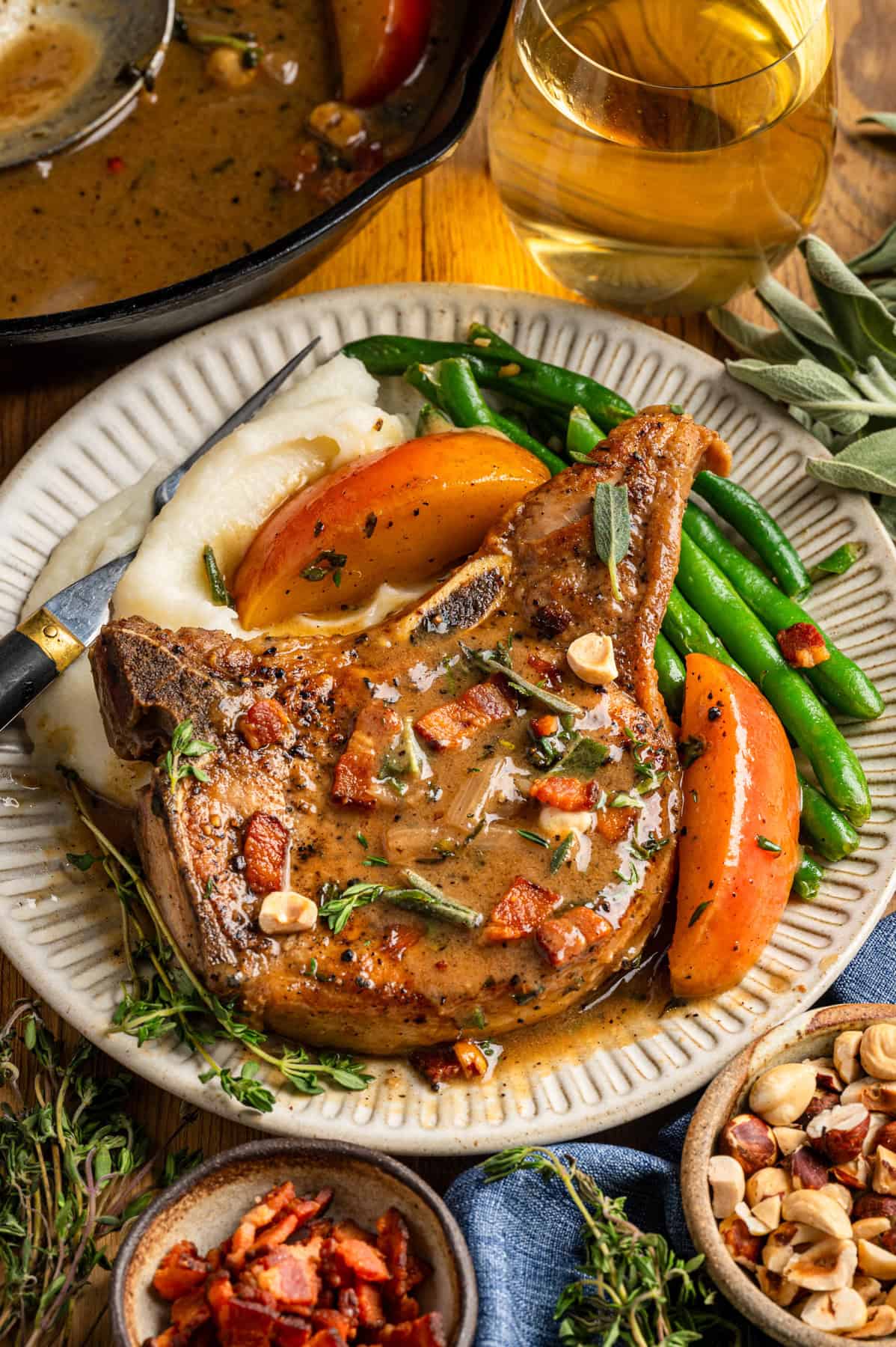 Apple Cider Pork Chops with Apples and Bacon Pork Chops with Apples, Bacon, Hazelnuts, green beans, and mashed potatoes - on a white plate.