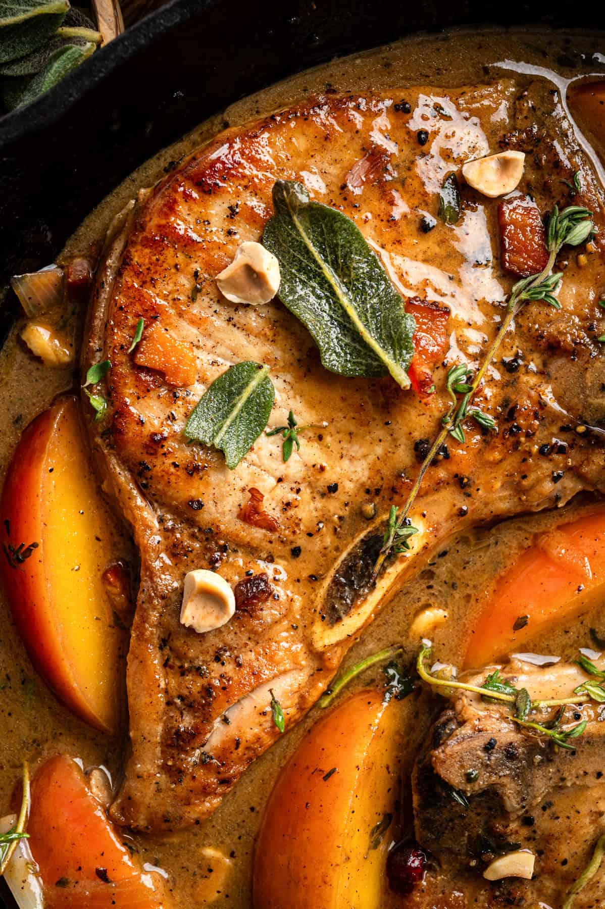 Apple Cider Pork Chops with Apples and Bacon Pork Chops with Apples, Bacon, and Hazelnuts in a black cast iron pan.