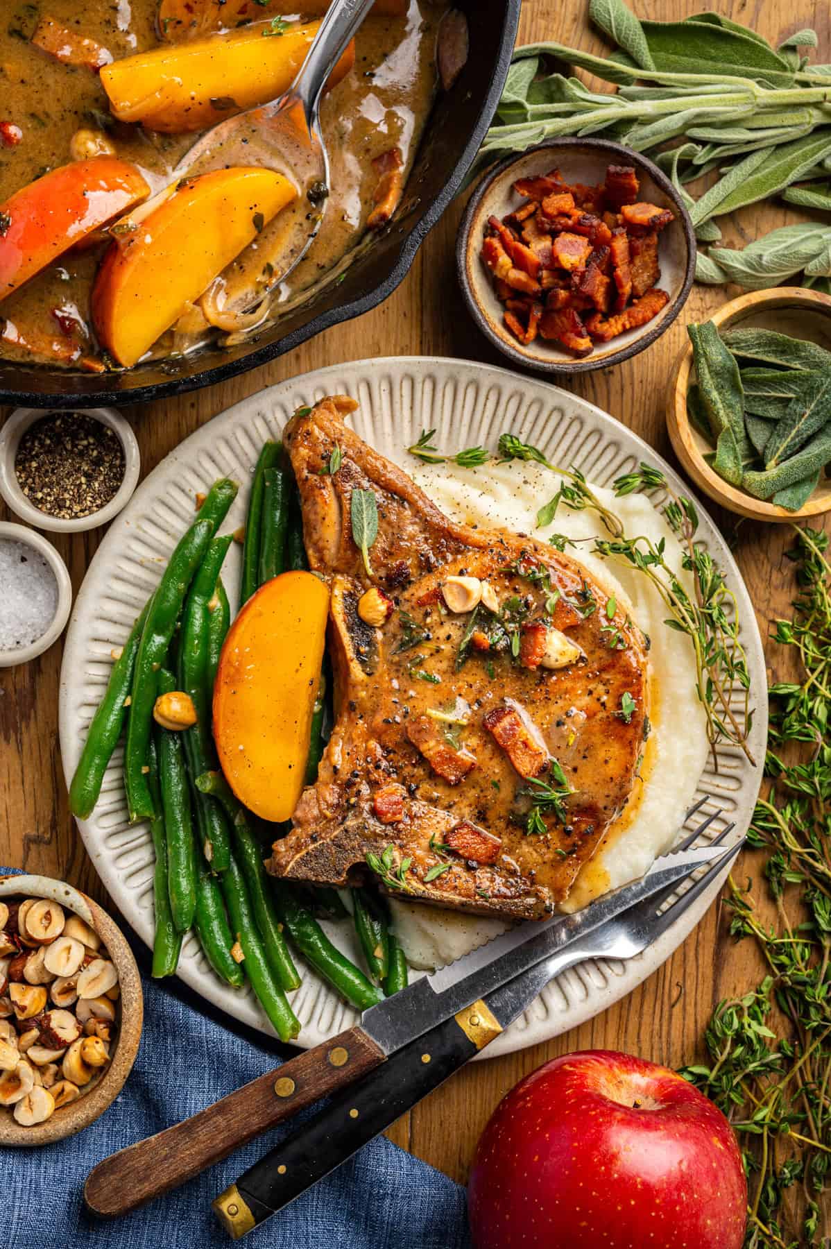 Apple Cider Pork Chops with Apples and Bacon Pork Chops with Apples, Bacon, Hazelnuts, green beans, and mashed potatoes - on a white plate.