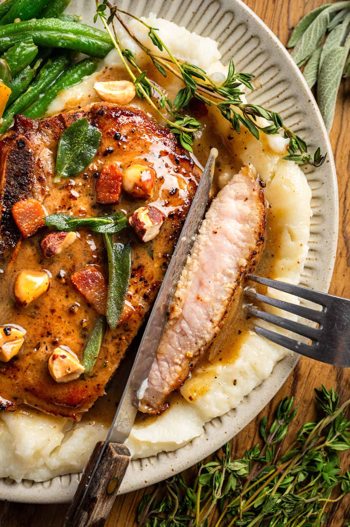 Apple Cider Pork Chops with Apples and Bacon Pork Chops with Apples, Bacon, Hazelnuts, green beans, and mashed potatoes - on a white plate.
