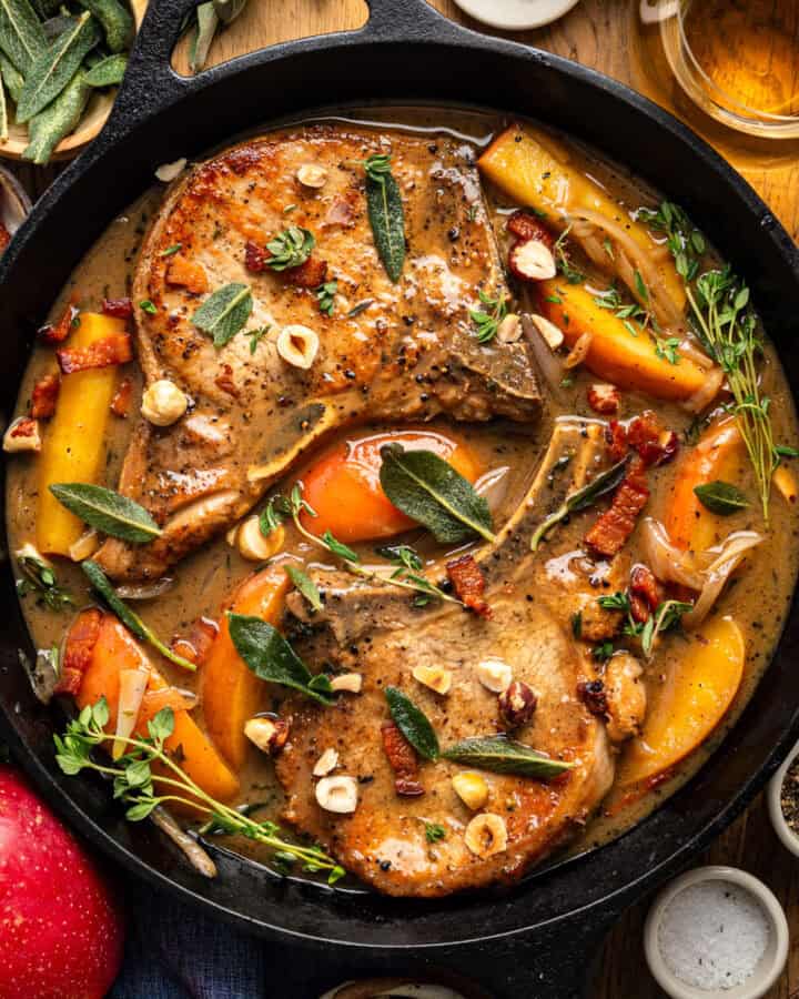 Pork Chops with Apples, Bacon, and Hazelnuts in a black cast iron pan.