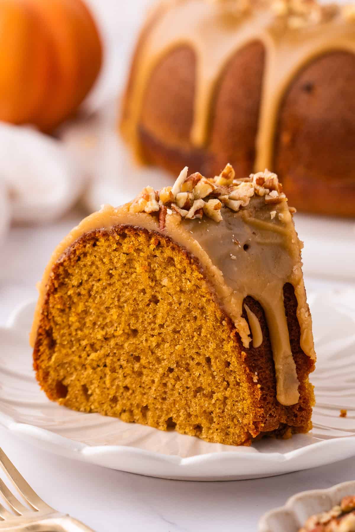 A slice of Pumpkin Bundt Cake Topped with Brown Sugar Glaze and Pecans - on a plate.