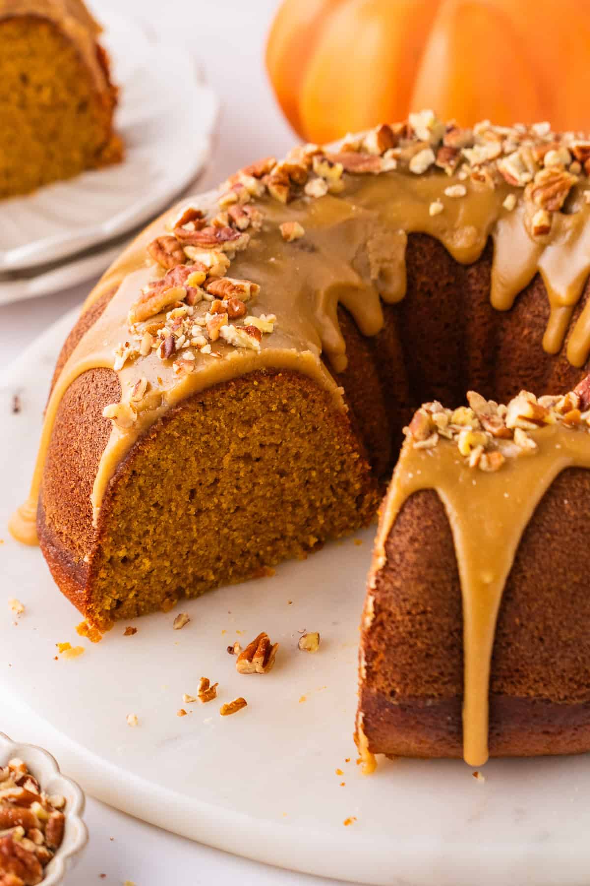 Pumpkin Bundt Cake Topped with Brown Sugar Glaze and Pecans, with a slice cut out.