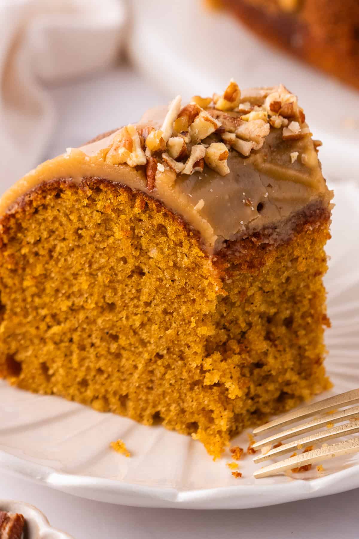 A sliced of Pumpkin Bundt Cake Topped with Brown Sugar Glaze and Pecans - on a plate.