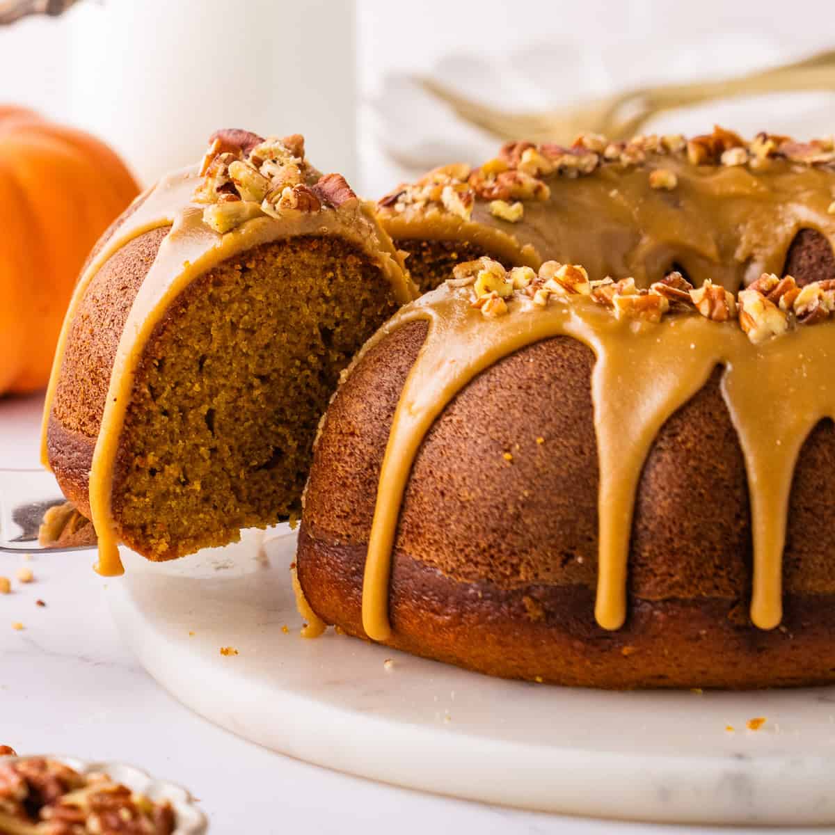 Pumpkin Bundt Cake Topped with Brown Sugar Glaze and Pecans, with a slice sliding out on a spatula.