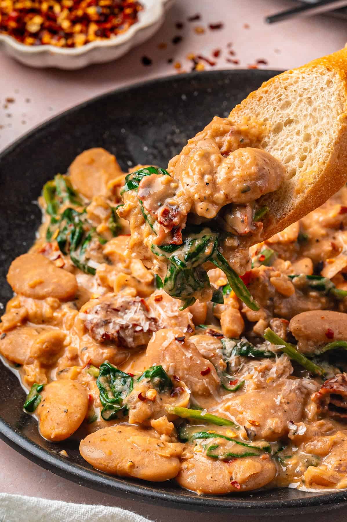 Tuscan Marry-Me Butter Beans with Spinach, Sun-Dried Tomatoes, and Parmesan Cheese - on a black plate.