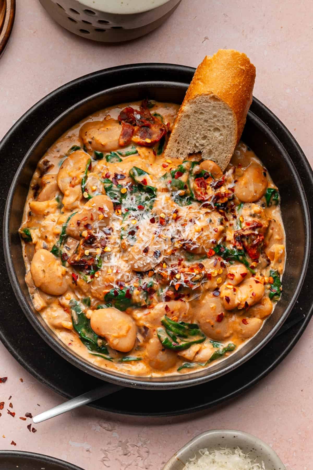 Tuscan Marry-Me Butter Beans with Spinach, Sun-Dried Tomatoes, and Parmesan Cheese - in a black bowl.