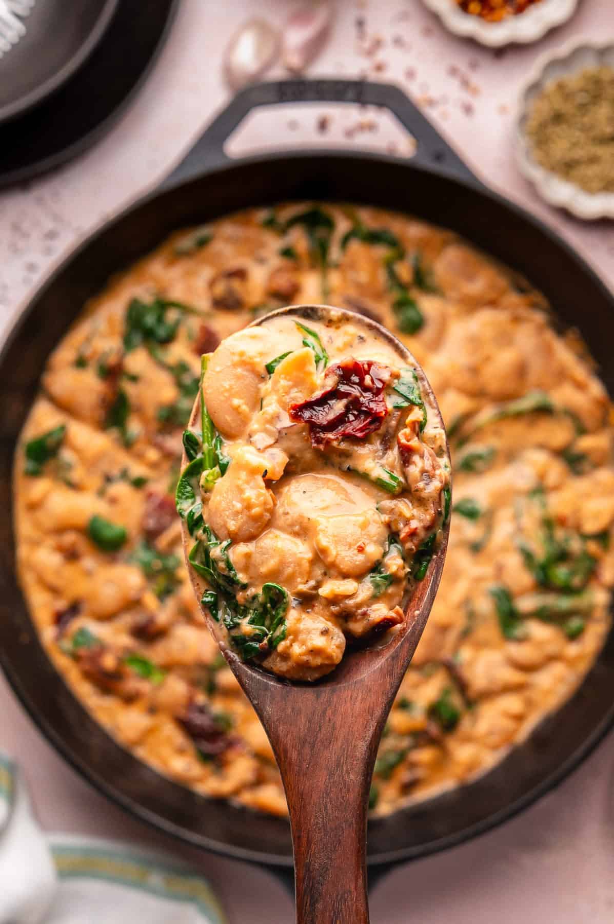 Close-up of Tuscan Marry-Me Butter Beans on a wooden spoon over the cast iron skillet.