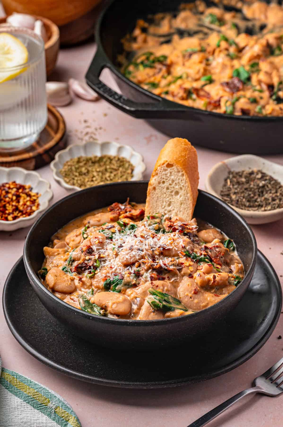 Tuscan Marry-Me Butter Beans with Spinach, Sun-Dried Tomatoes, and Parmesan Cheese - in a black bowl.