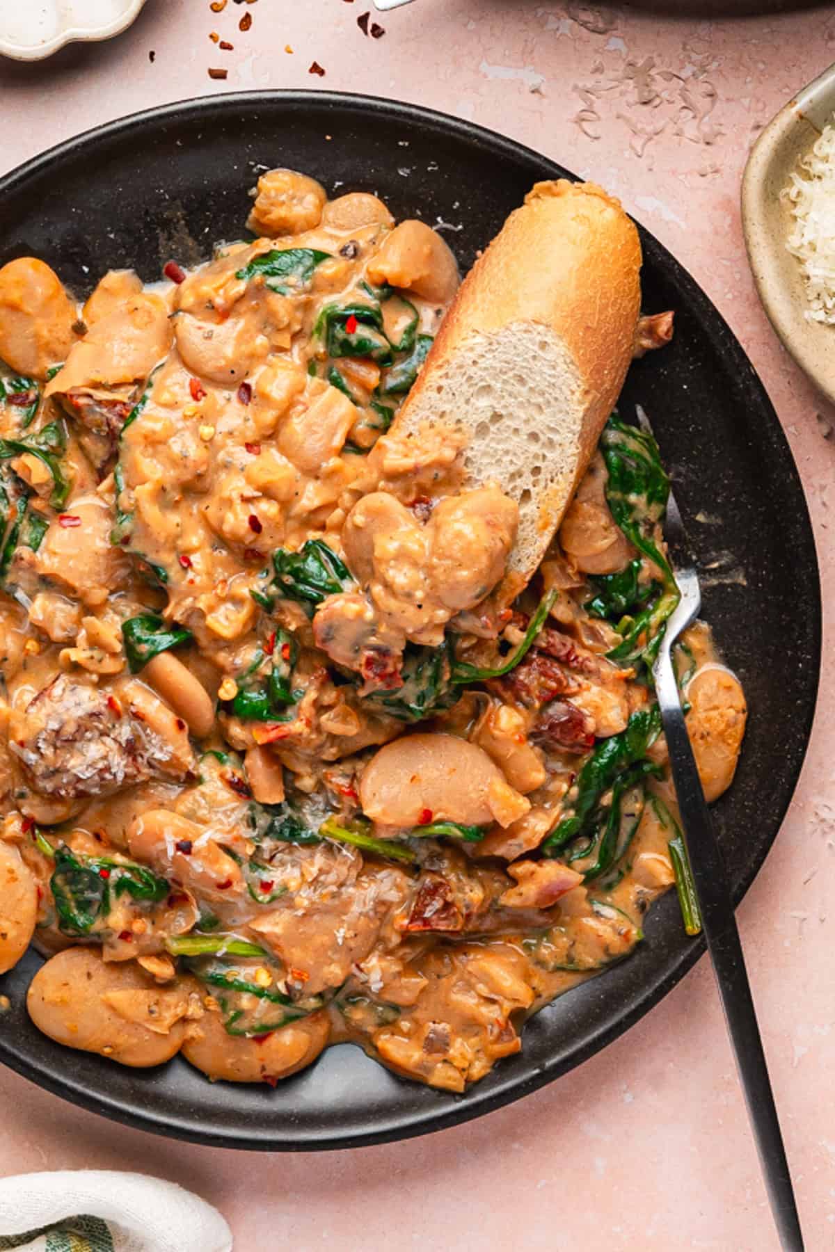 Tuscan Marry-Me Butter Beans with Spinach, Sun-Dried Tomatoes, and Parmesan Cheese - on a black plate.