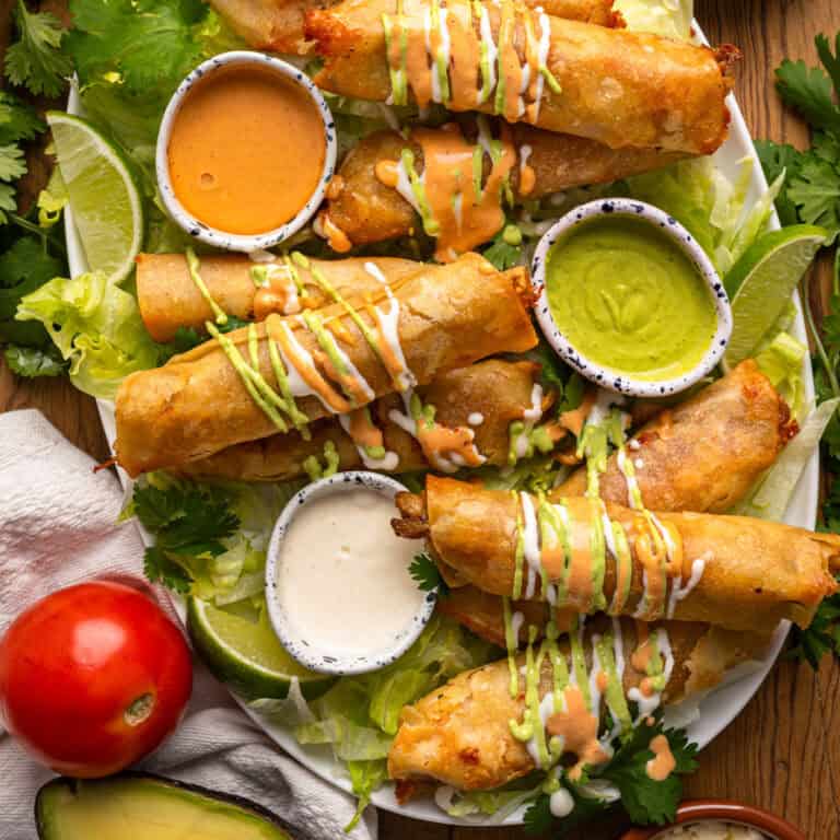Chicken Taquitos (drizzled with 3 different sauces) on a platter (with each sauce in small bowls).