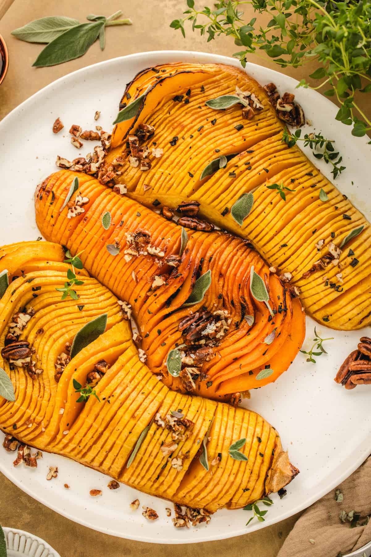 Hasselback Butternut Squash topped with chopped pecans and sage leaves (3 squash halves on a white platter).