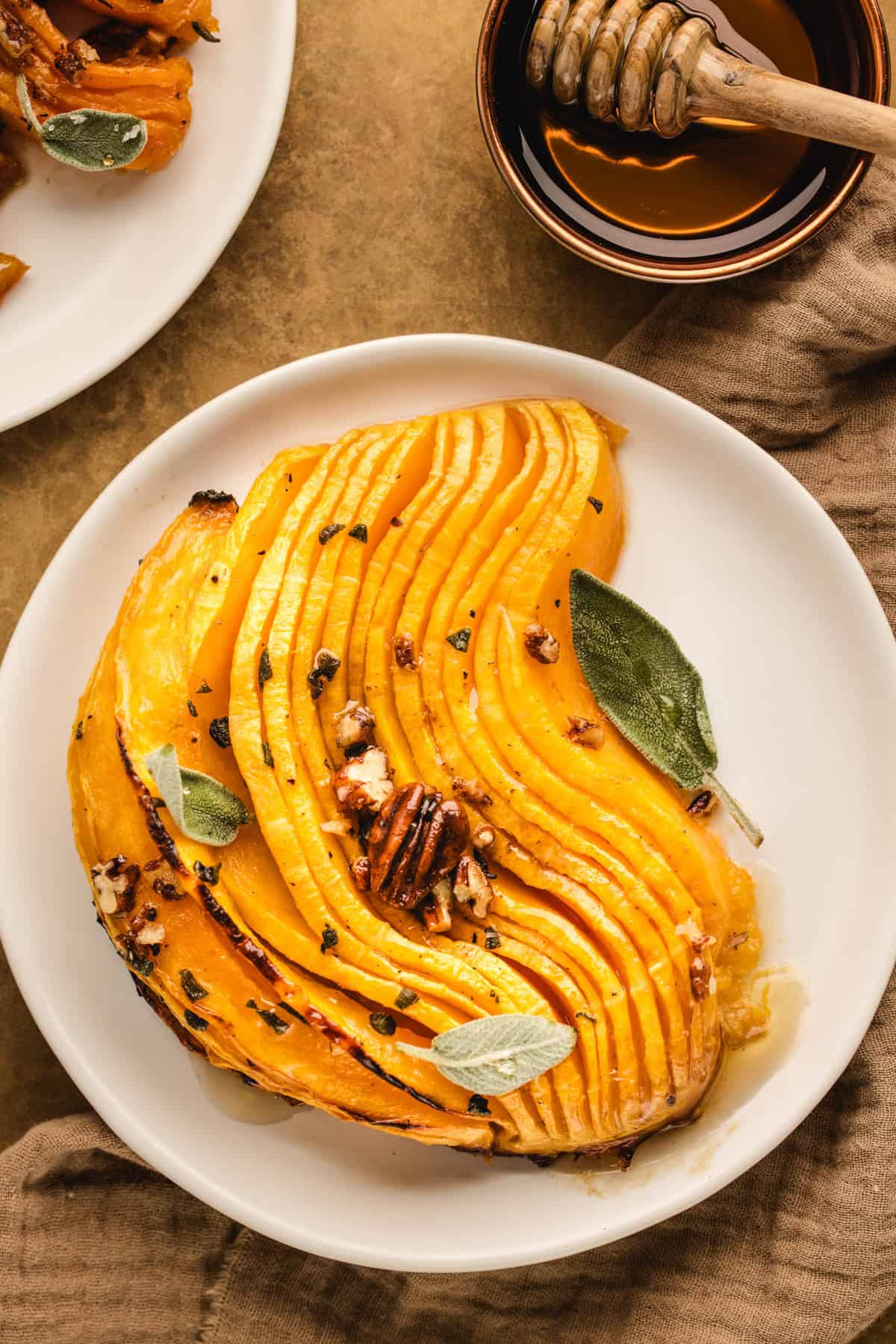 A slice of Hasselback Butternut Squash (topped with pecans and sage leaves) on a small plate.