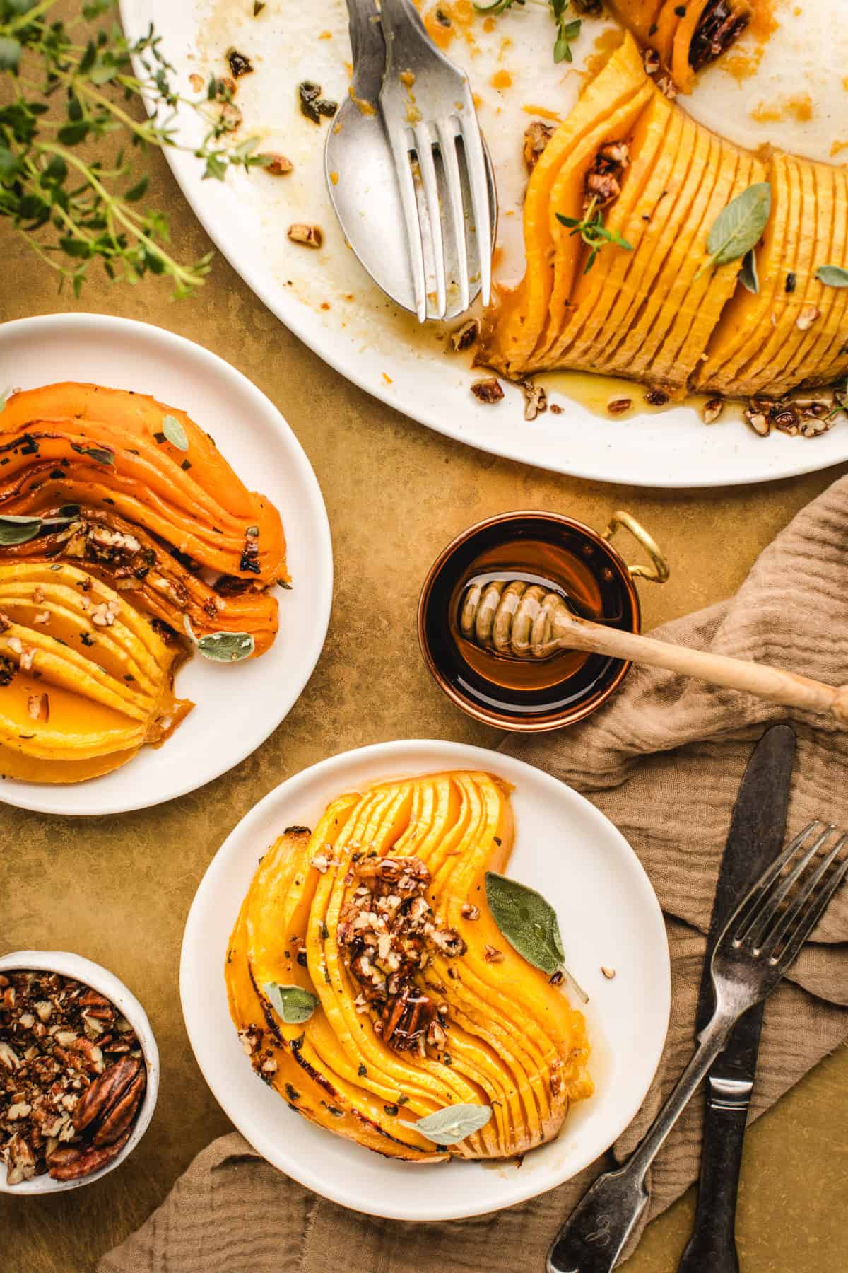 Overhead view of 3 plates with Hasselback Butternut Squash topped with chopped pecans.