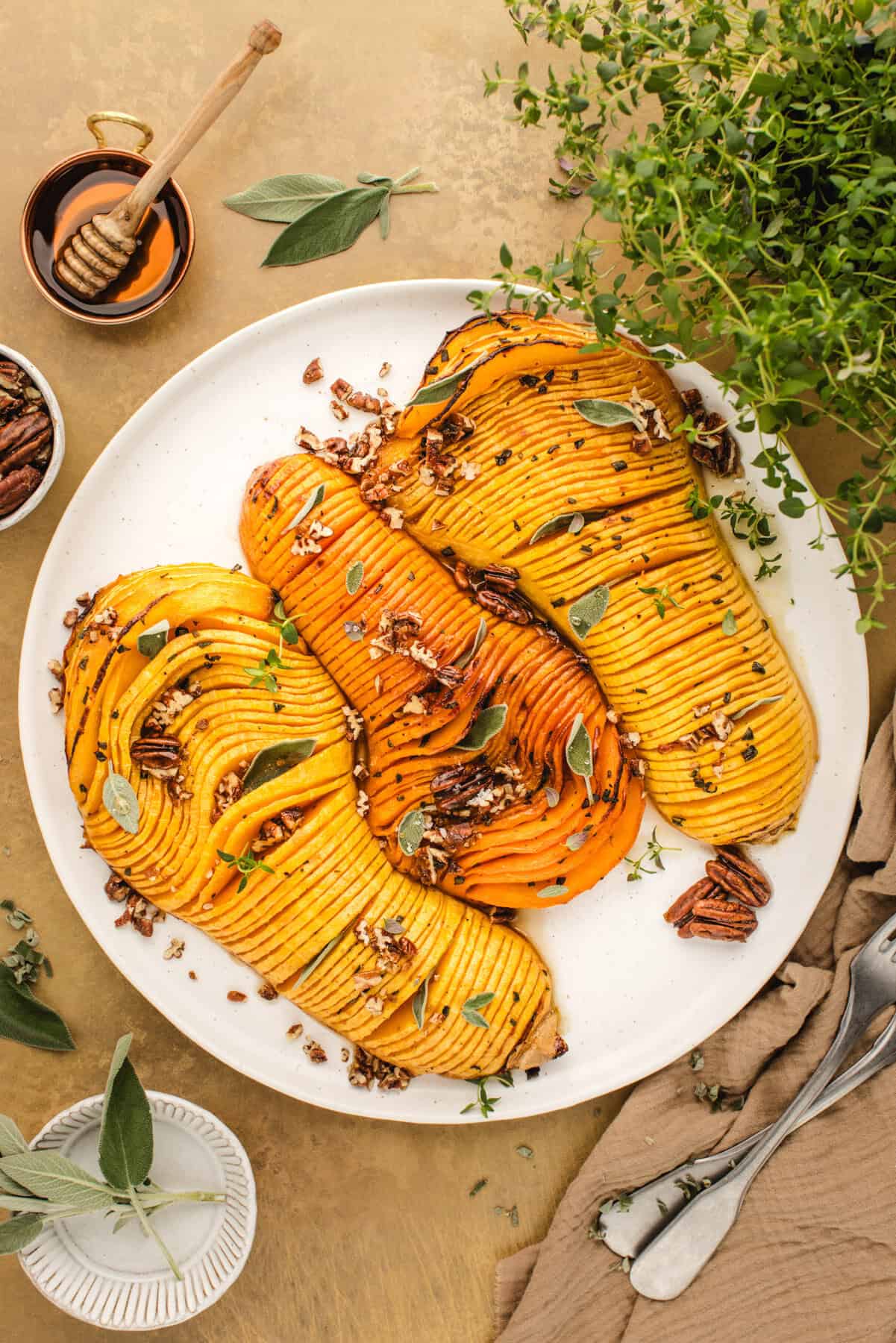 Hasselback Butternut Squash topped with chopped pecans and sage leaves (3 squash halves on a white platter).
