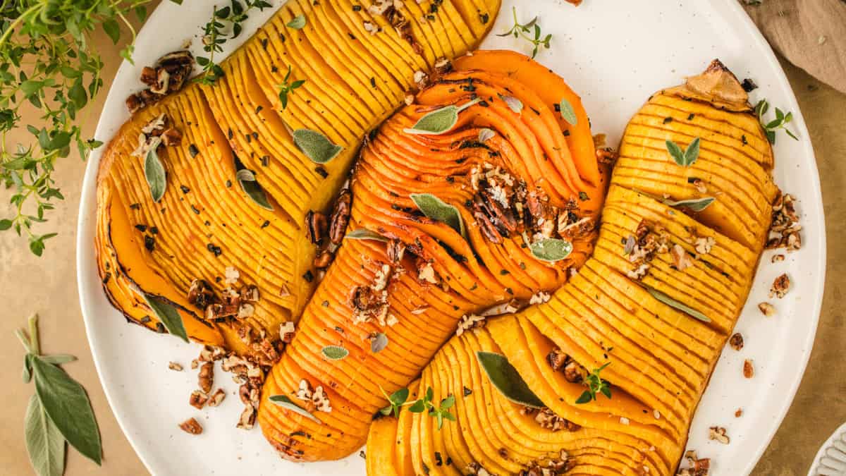 Hasselback Butternut Squash topped with chopped pecans and sage leaves (3 squash halves on a white platter).