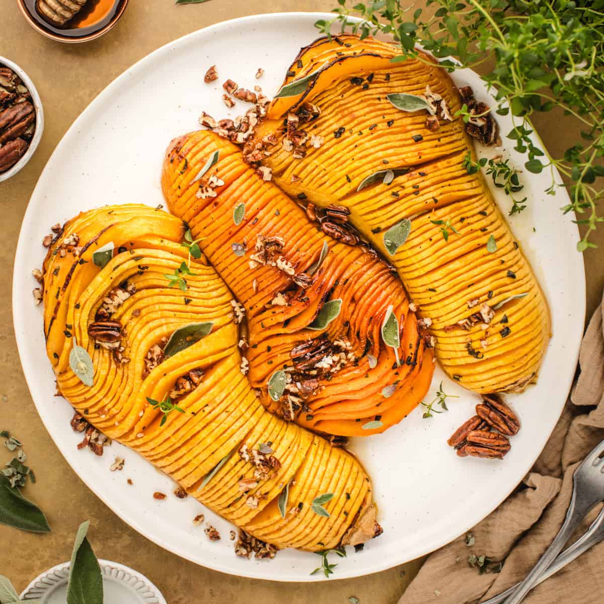 Hasselback Butternut Squash topped with chopped pecans and sage leaves (3 squash halves on a white platter).