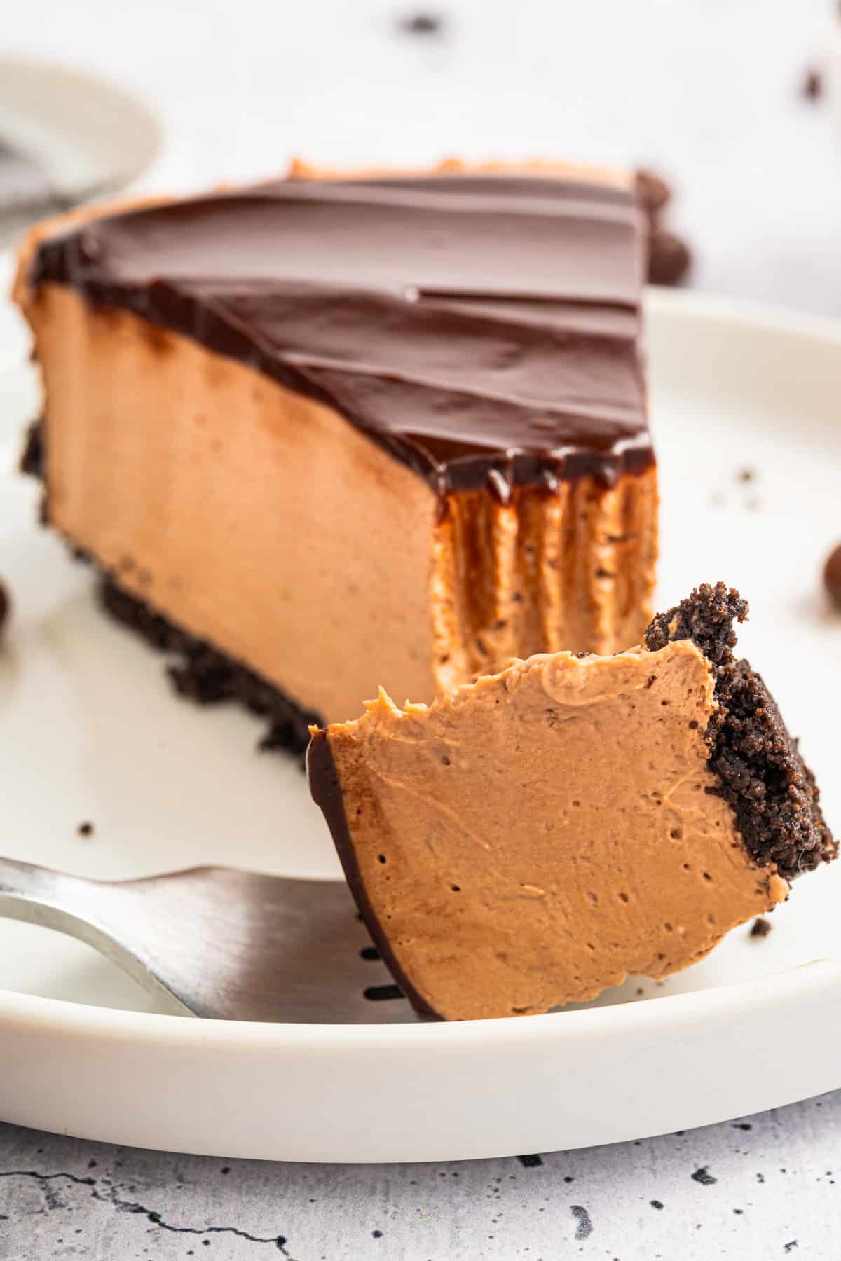 A slice of Mocha Cheesecake on a plate, with a big cake chunk sliced off by a fork.