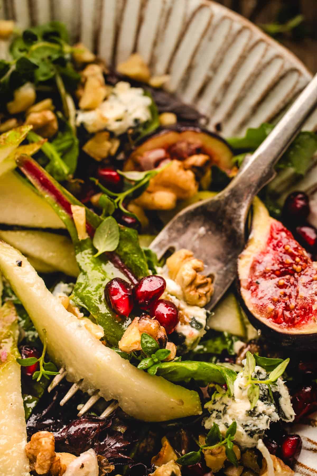 Pear Salad with Walnuts, Blue Cheese, Mixed Greens,  Pomegranate, Figs, and Honey-Dijon Dressing - in a bowl, with a fork (close-up shot)