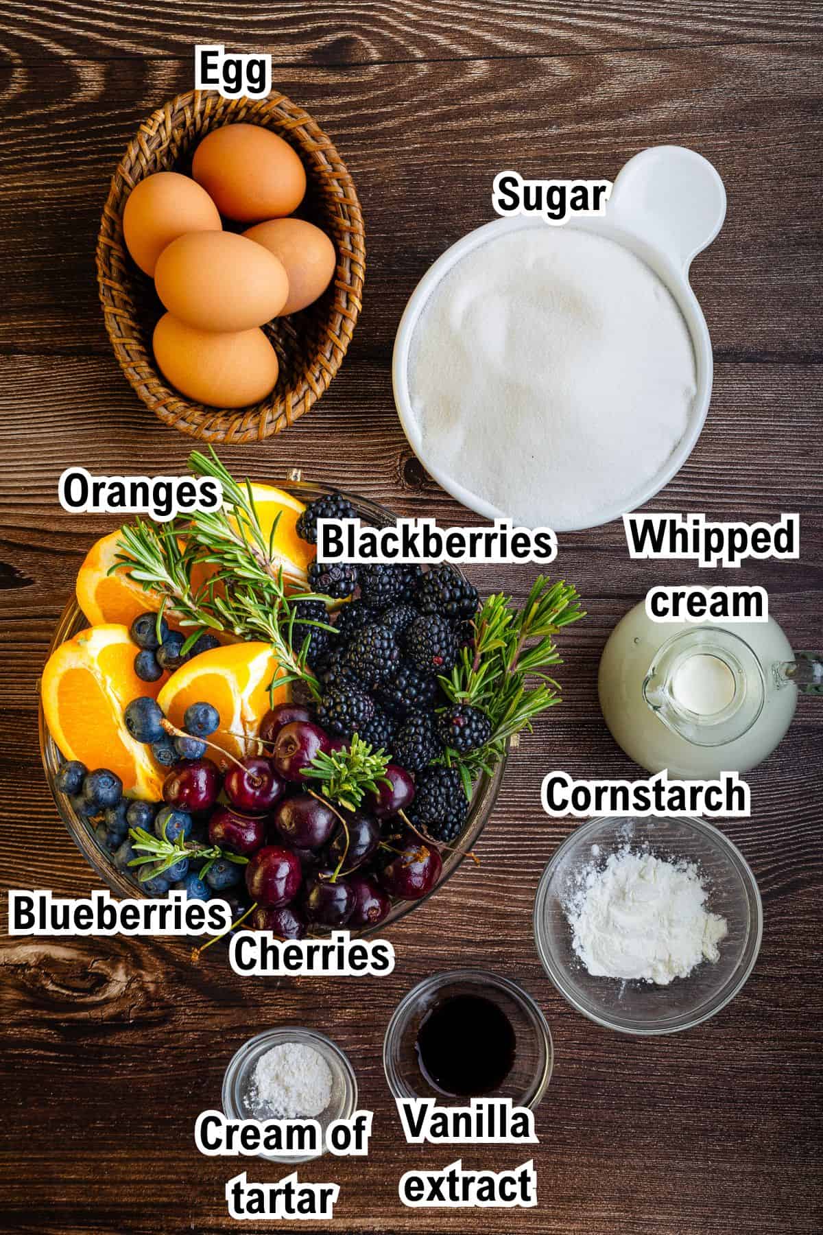 This photo shows the ingredients for Berry Pavlova: Eggs, sugar, oranges, blackberries, blueberries, cherries, whipped cream, cornstarch, cream of tartar, and vanilla extract on a wooden table.