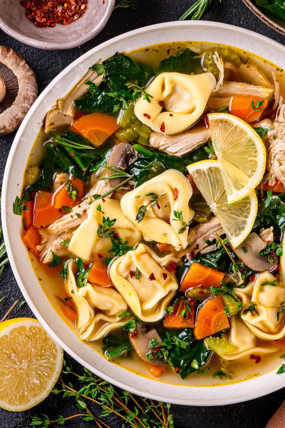 Chicken tortellini soup with spinach, carrots, mushrooms, and lemon - in a white bowl.