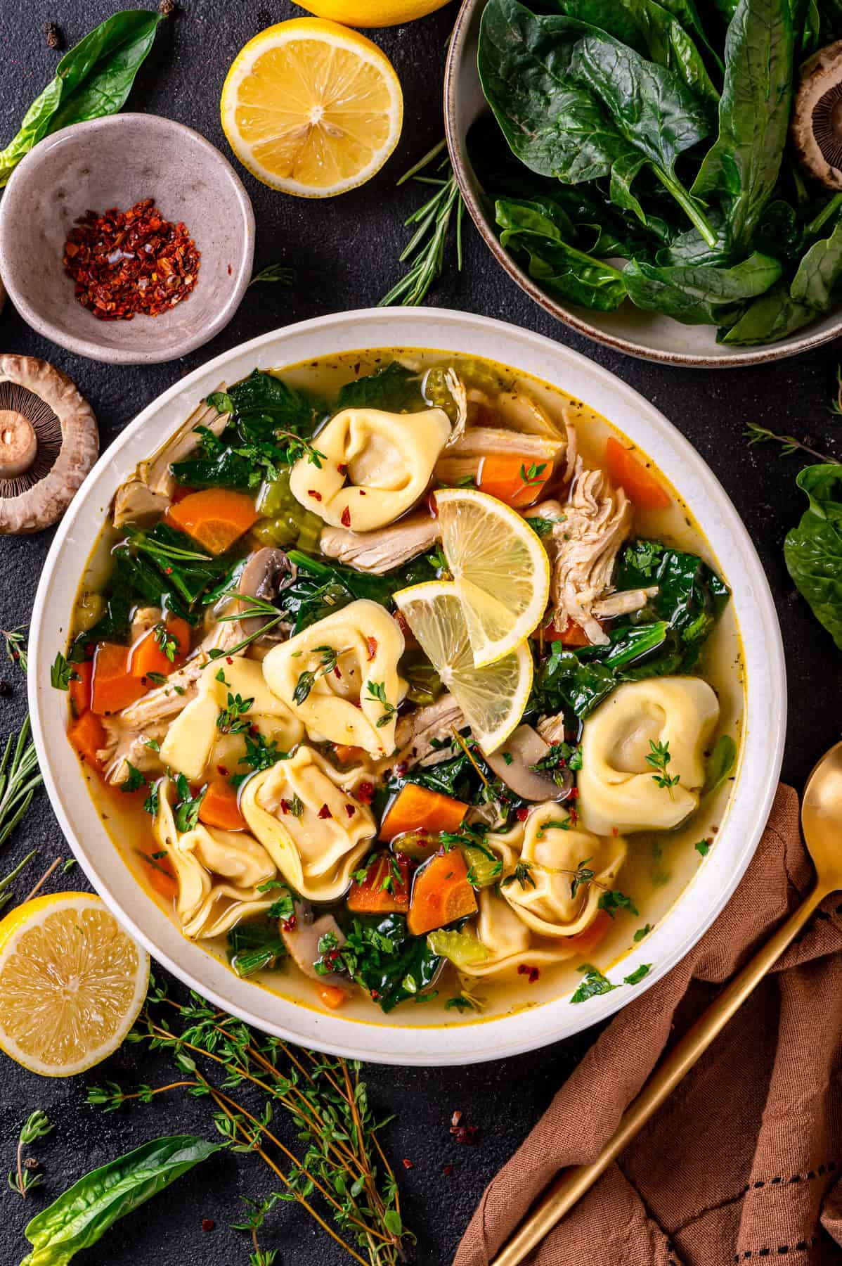 Chicken tortellini soup with spinach, carrots, mushrooms, and lemon - in a bowl.
