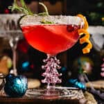 Christmas Cranberry Mimosa in a glass with sugared rim, garnished with sugared rosemary, orange peel twist, and fresh cranberries.