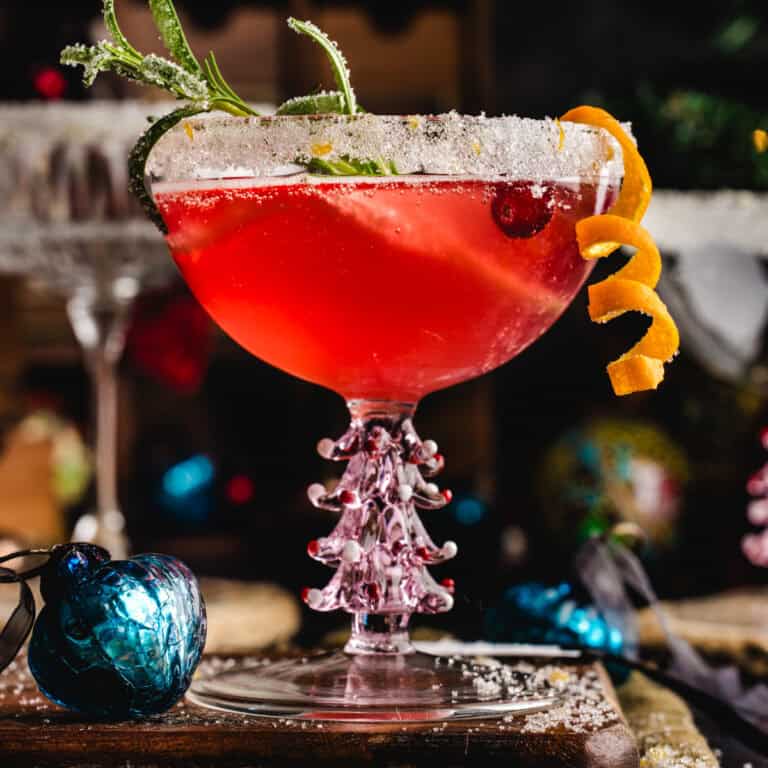 Christmas Cranberry Mimosa in a glass with sugared rim, garnished with sugared rosemary, orange peel twist, and fresh cranberries.