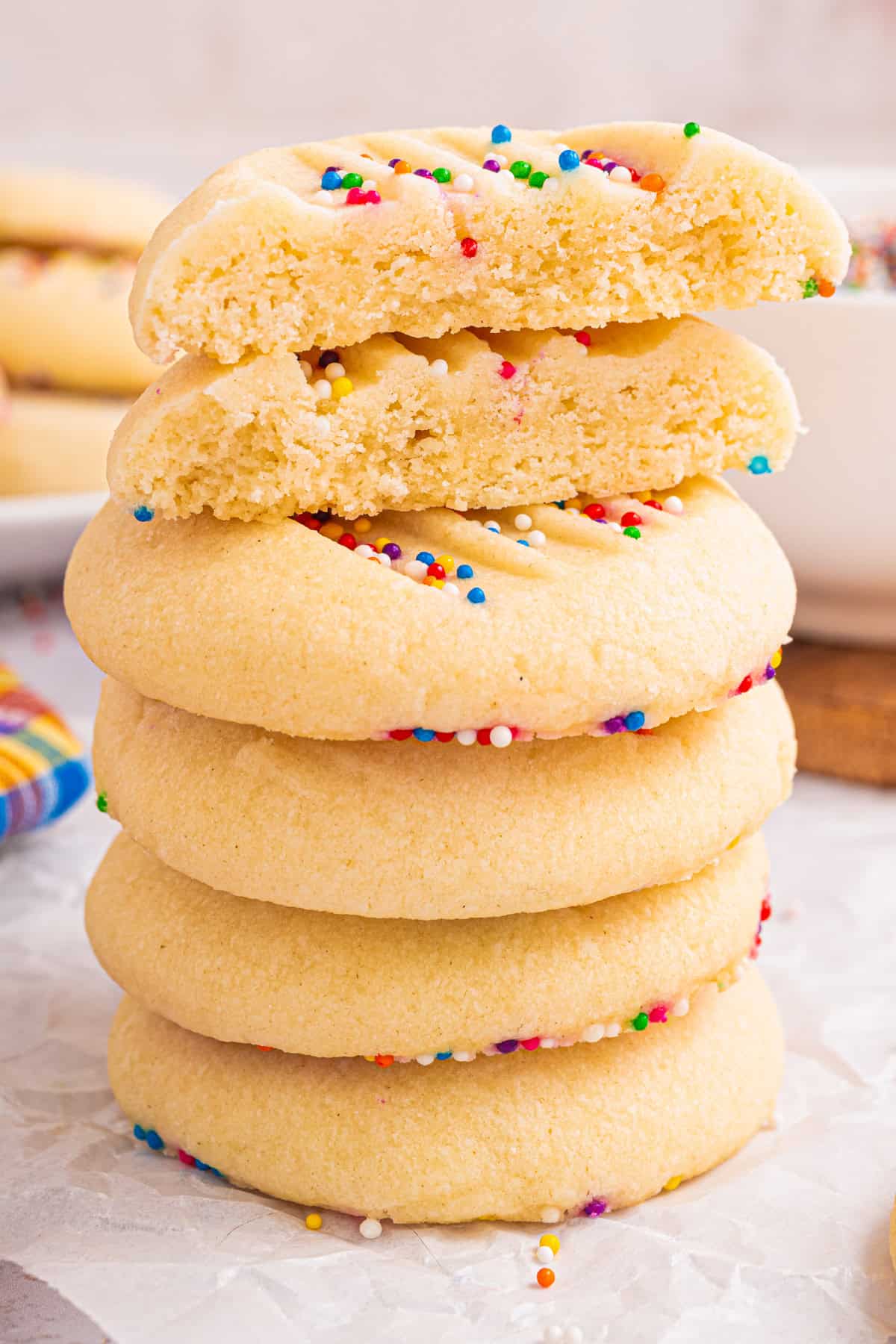 A tall stack of Whipped Shortbread Cookies with sprinkles, with the top two cookies broken in half.