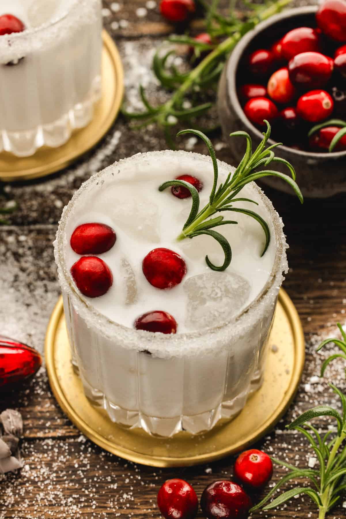 White Christmas Margarita in a glass, garnished with fresh cranberries and a rosemary sprig.