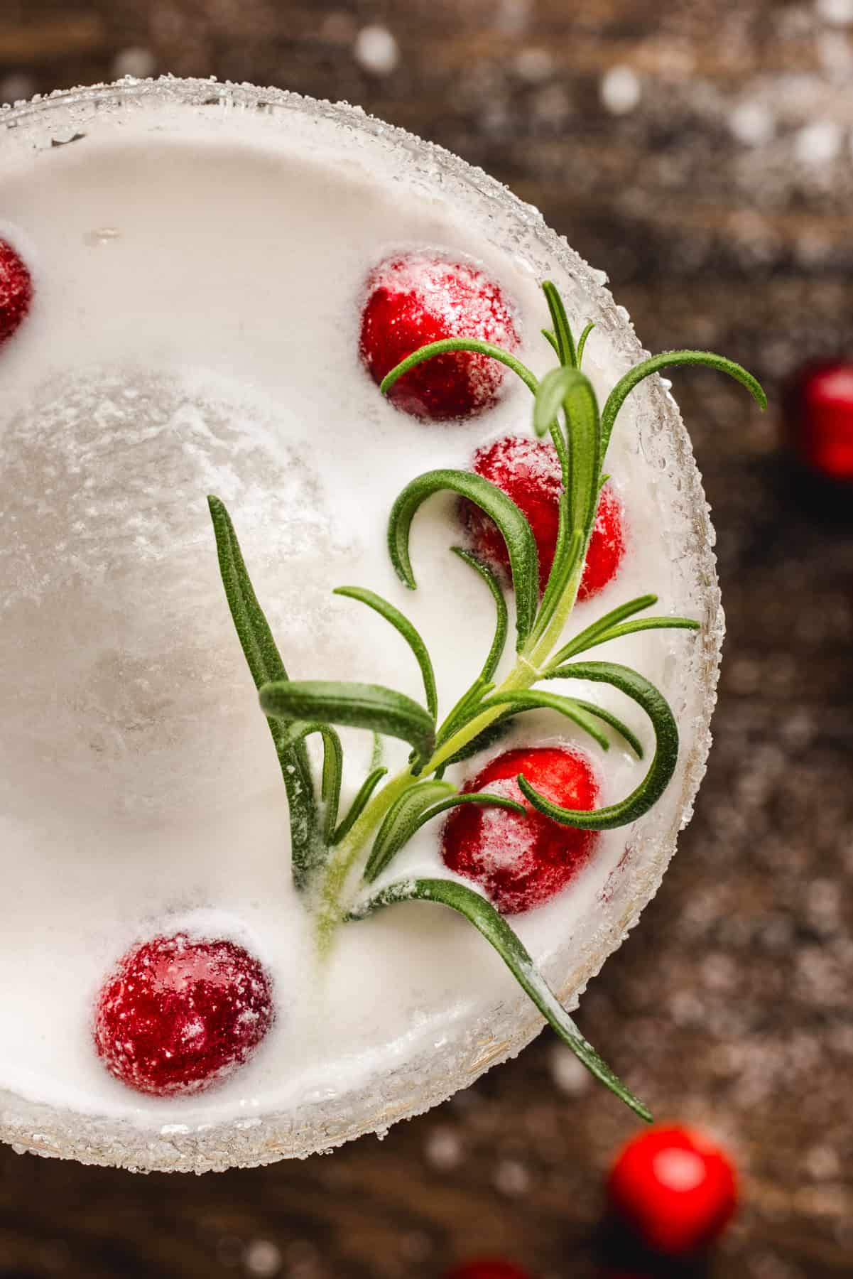 White Christmas Margarita in a glass, garnished with fresh cranberries and a rosemary sprig.
