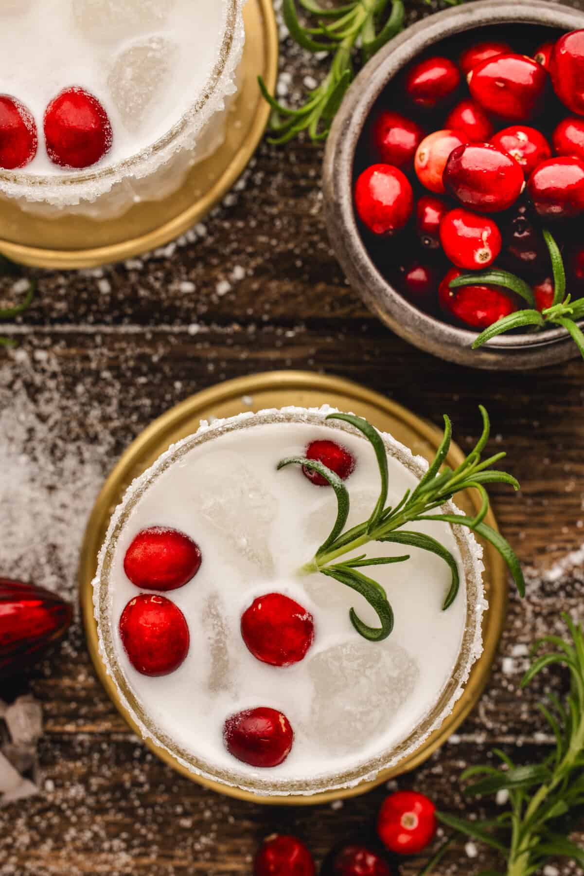White Christmas Margarita in a glass, garnished with fresh cranberries and a rosemary sprig.