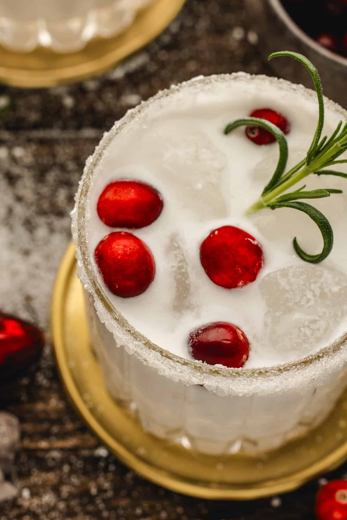 White Christmas Margarita in a glass, garnished with fresh cranberries and a rosemary sprig.