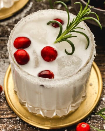 White Christmas Margarita in a glass, garnished with fresh cranberries and a rosemary sprig.