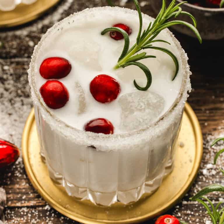 White Christmas Margarita in a glass, garnished with fresh cranberries and a rosemary sprig.