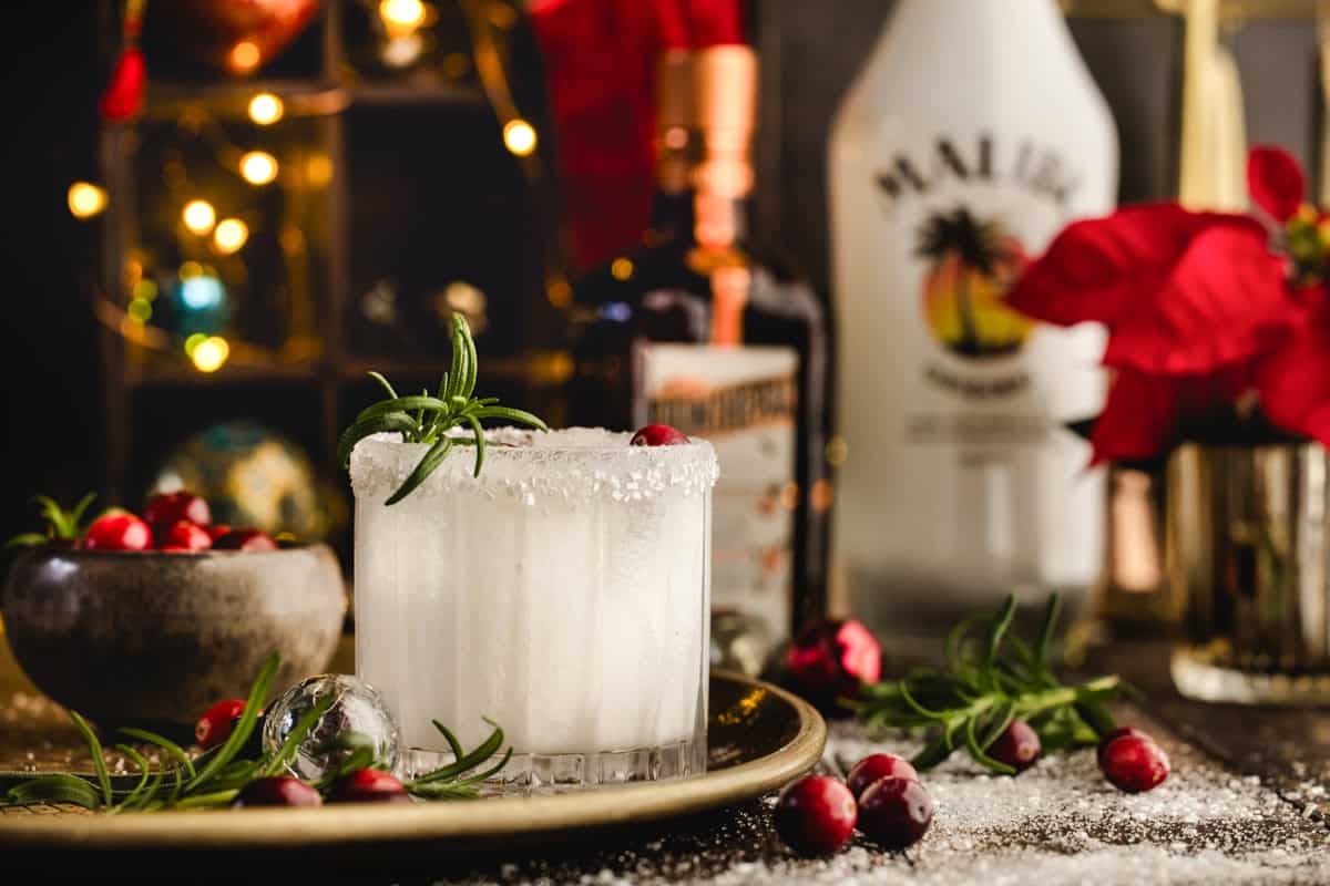 White Christmas Margarita in a glass on a tray with the alcohol bottles behind it as a background.
