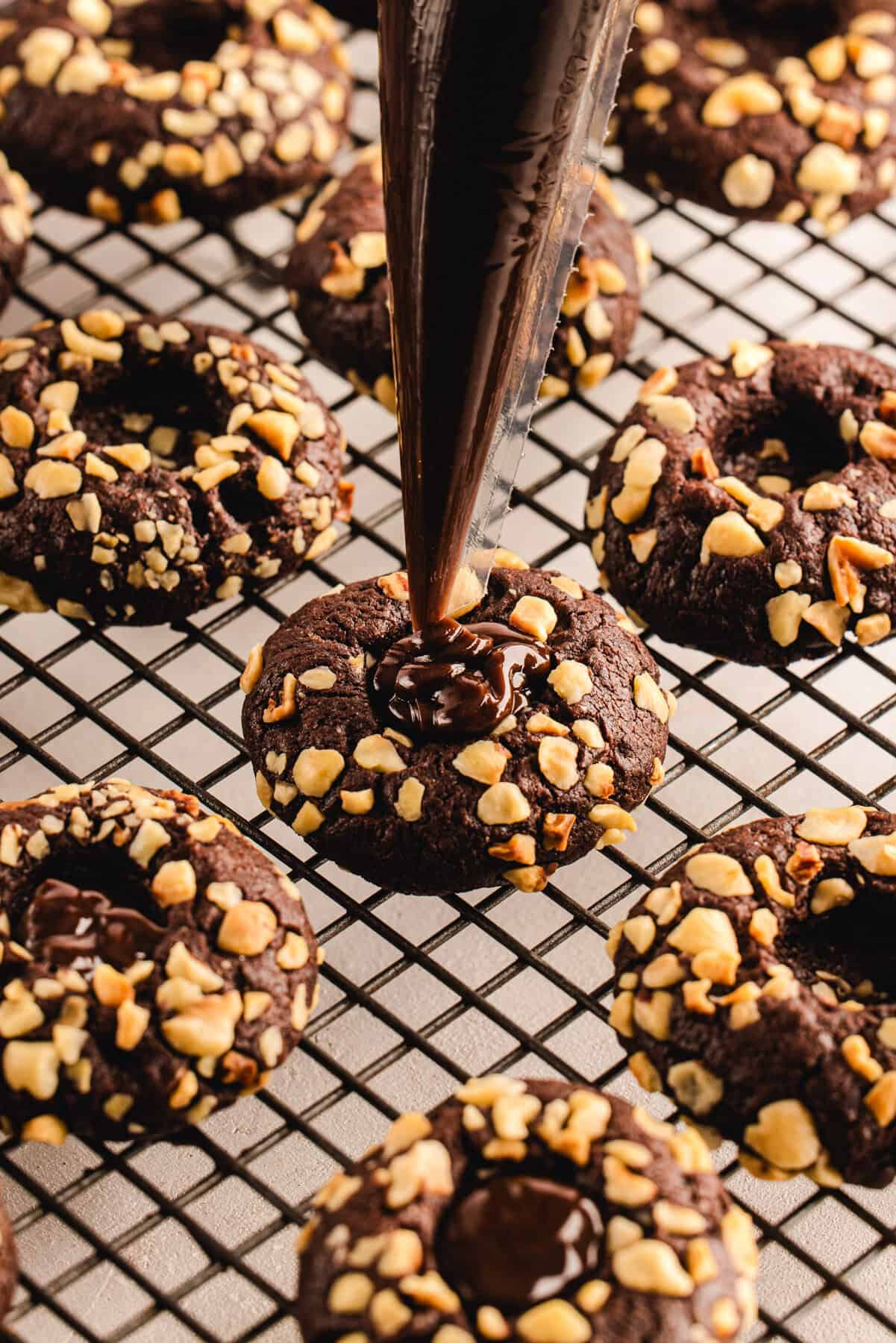 Chocolate Hazelnut Thumbprint Cookies piping Nutella filling on top of the Chocolate Hazelnut Thumbprint Cookies with a piping bag.