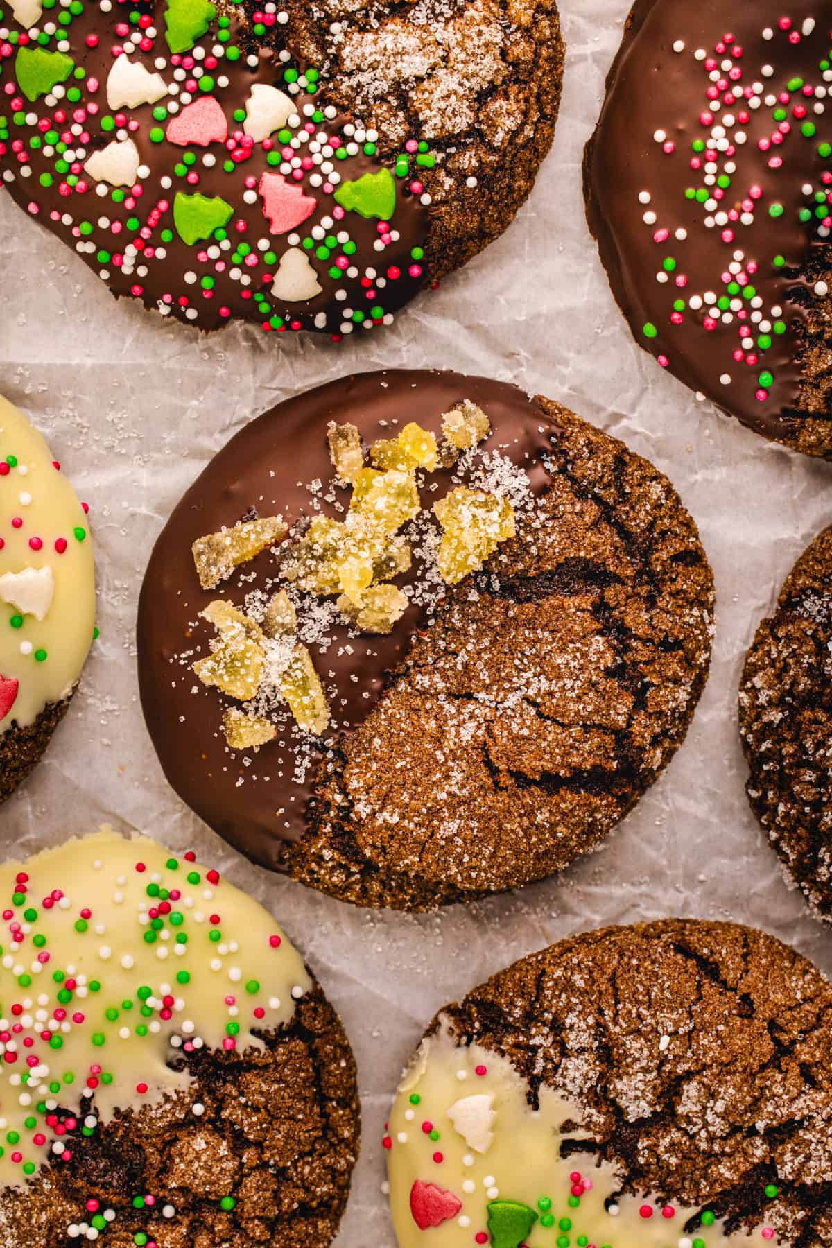 Ginger molasses cookie dipped in dark chocolate and topped with crystallized ginger in the center of other cookies on a white background.